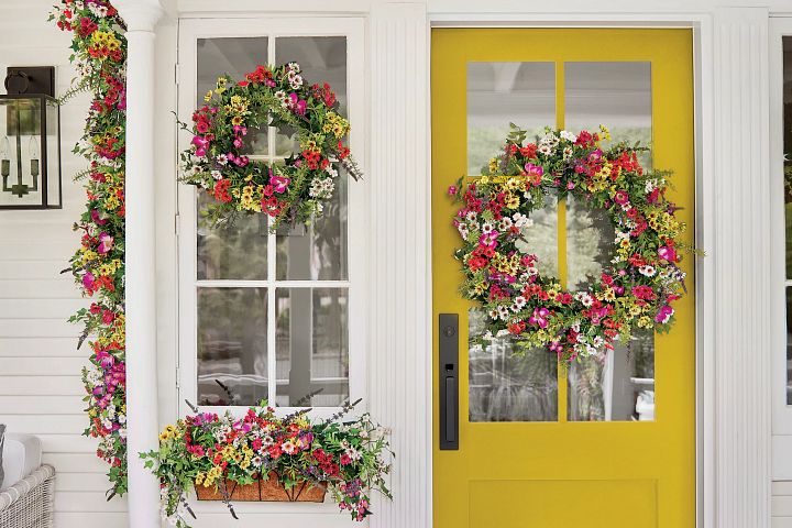 Yellow front door decorated with colorful spring wreath, garland, and window box