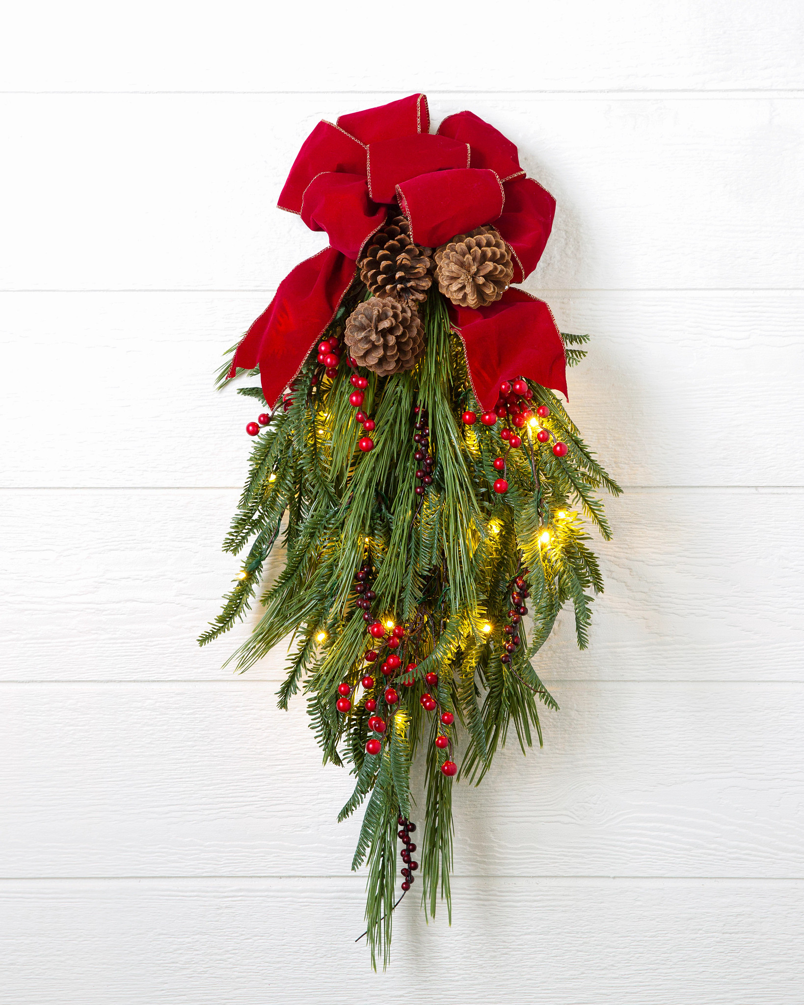 Artificial Christmas swag decorated with pinecones, berries, lights, and a red bow