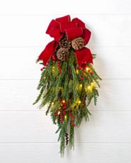 Artificial Christmas swag decorated with pinecones, berries, lights, and a red bow