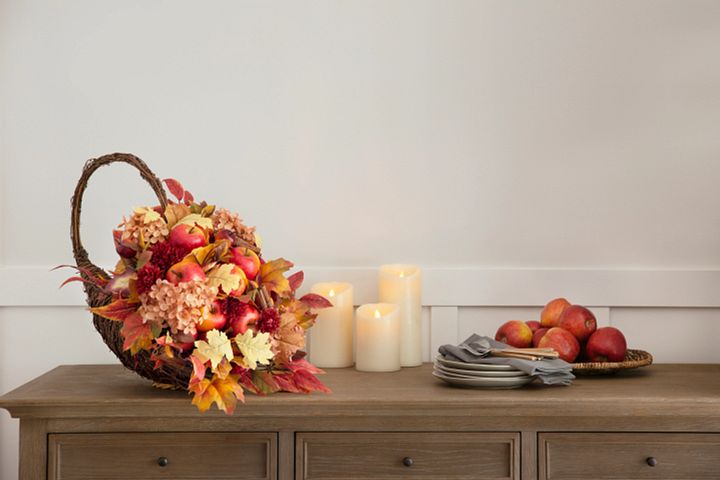 A cornucopia of apples and maple leaves next to a group of candles, a plate of fresh apples, and cutlery