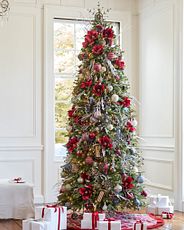 Sapin décoré de boules de Noël rustiques et de fleurs rouges.