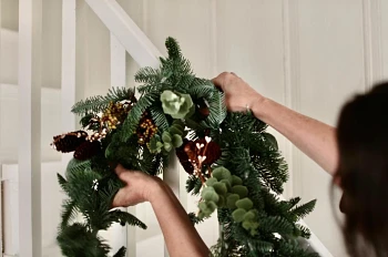 Woman hanging artificial Christmas wreath on staircase handrail