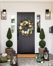 Entryway decorated with a pumpkin wreath, topiaries, and lanterns
