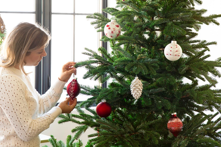 Woman placing red and white ornaments on a Balsam Hill artificial Christmas tree