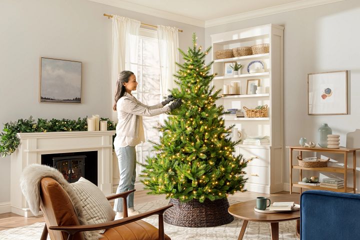 A woman shaping a pre-lit Christmas tree in a living room