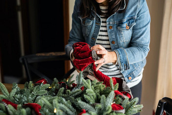 A woman tucking red velvet ribbon into a Christmas wreath