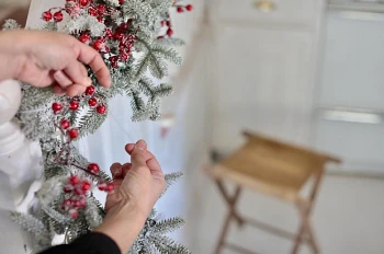 Woman tying artificial Christmas garland to stair banister with nylon cord