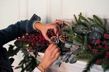 Hands adding pinecones to artificial Christmas garland