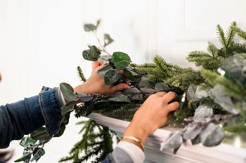 Hands adding eucalyptus picks to Christmas garland