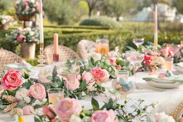 Outdoor dining setup with pink glower garlands, hanging baskets, candles, and tableware