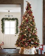 Artificial Christmas tree decorated with burgundy and gold ornaments, silver and gold tree garlands, and capiz tree collar