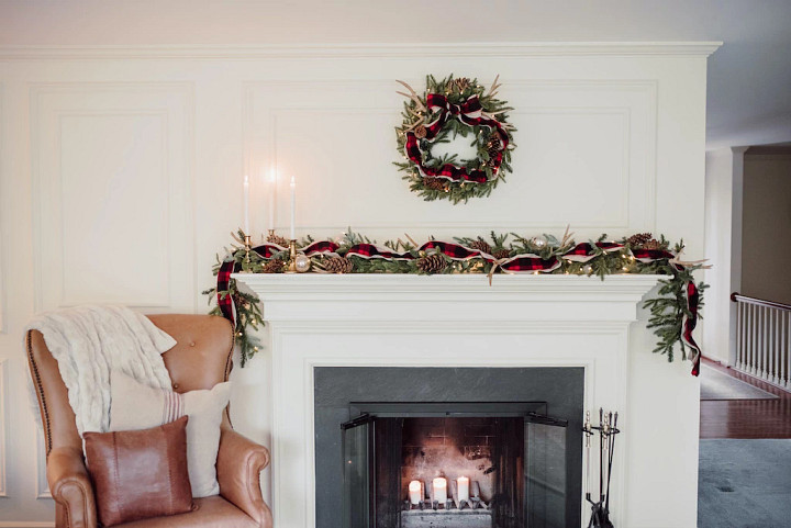 A fireplace mantel decorated with a wreath and garland in a cozy cabin Christmas decorating theme