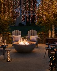 Outdoor seating area and firepit decorated with lanterns with fairy lights and string lights hanging from trees