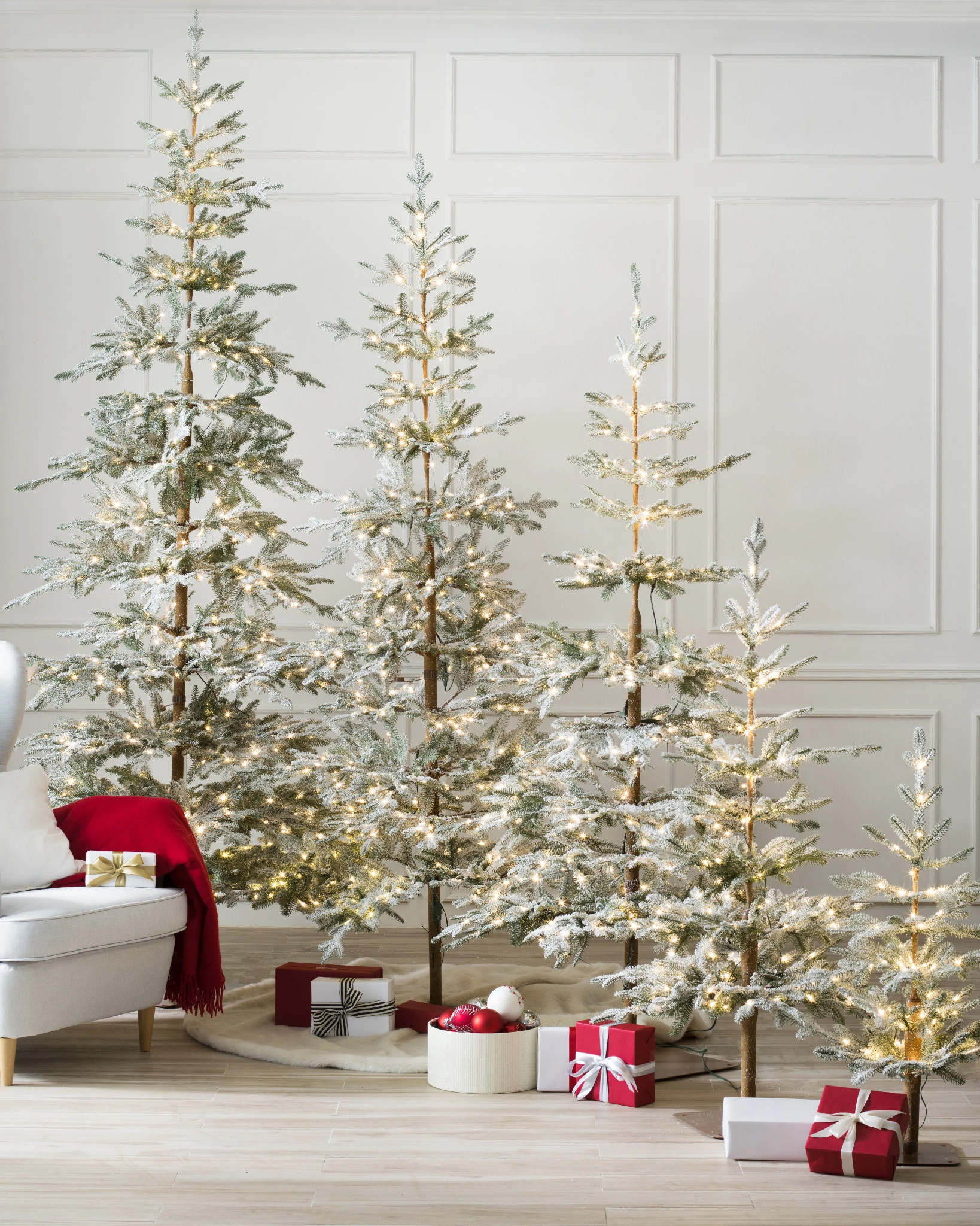 A group of pre lit frosted Christmas trees with sparse branches, softly glowing and arranged to create a simple, wintry display.