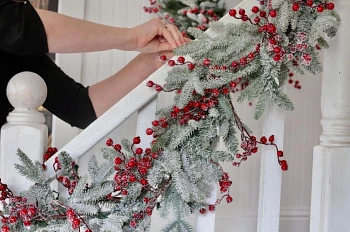 Hands tying artificial frosted Christmas garland with red berries to banister