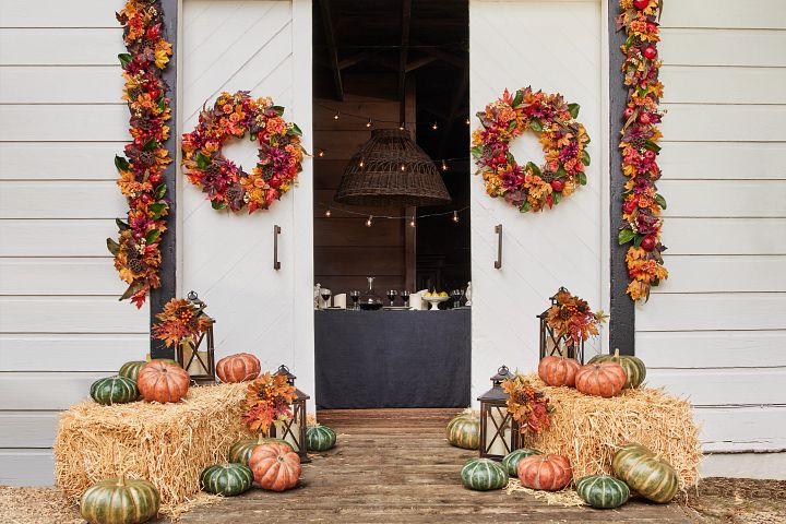 Entrance decorated with fall foliage, artificial pumpkins, and candles in lanterns