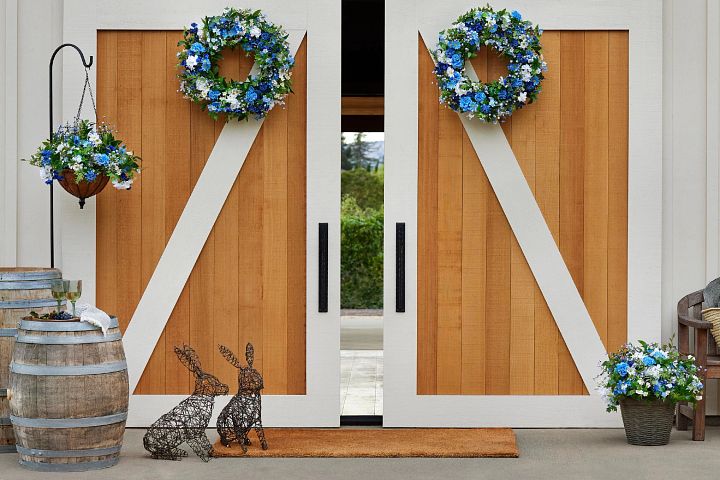 Outdoor barn doors decorated with blue-and-white artificial spring greenery and a pair of wired bunny sculptures