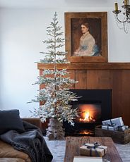 A sparse artificial Christmas tree next to a lit wooden mantel