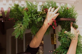 Pair of hands hanging an artificial Christmas garland from a metal hanger on the door frame