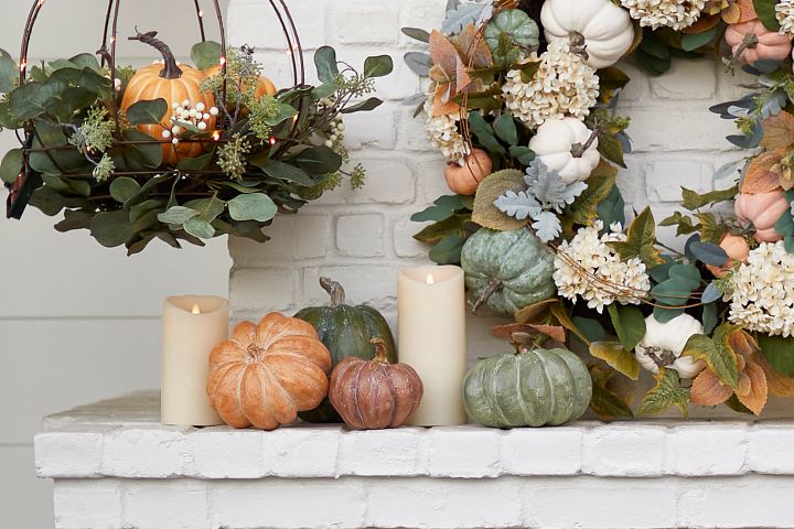 White brick mantel decorated with artificial eucalyptus wreath and hanging basket, pumpkins, and candles