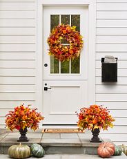 Front door decorated with autumn wreath, potted arrangements, and pumpkins
