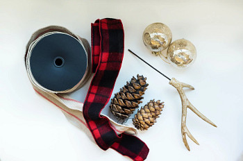 Flatlay of wreath decorating supplies such as jute ribbon, buffalo check ribbon, pinecones, antlers, gold ball ornaments