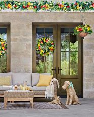 Outdoor seating area decorated with red and yellow artificial flower garlands, wreaths, and hanging baskets