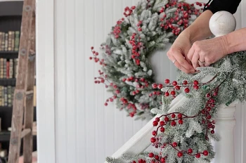 Hand tying artificial Christmas garland with nylon cord to top of stair banister