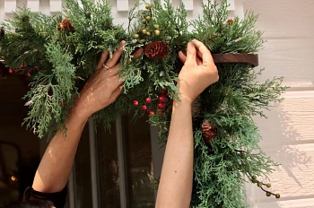 Pair of hands fluffing foliage of artificial Christmas garland hanging from a metal hanger
