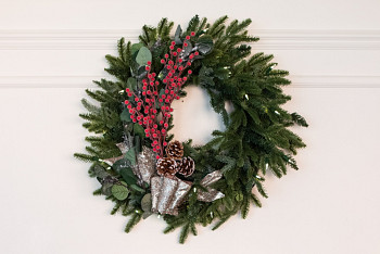 A Christmas wreath decorated with frosted red berry picks, frosted eucalyptus leaves, pinecones, and champagne glittered Christmas tree ribbon