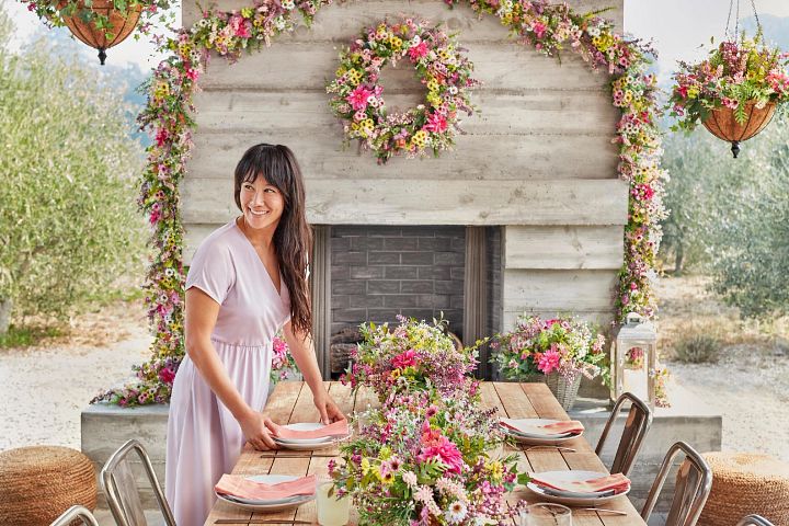 Woman setting up an outdoor dining table with artificial spring flowers and place settings