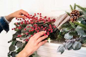 Hands fixing red berry decorations on a Christmas garland