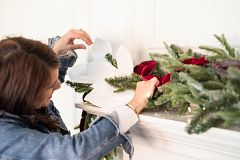 Frau schmückt künstliche Weihnachtsgirlande mit Bändern und Zweigspitzen