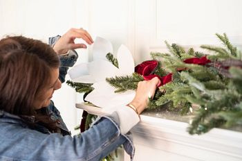 Woman decorating artificial Christmas garland with ribbons and picks