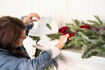 A woman decorating a Christmas garland with white magnolia branch picks