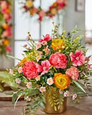 Artificial flower arrangement with faux cottage roses, ranunculus, peonies, billy buttons, cosmos, eucalyptus, and fern leaves set in a gold ceramic pot