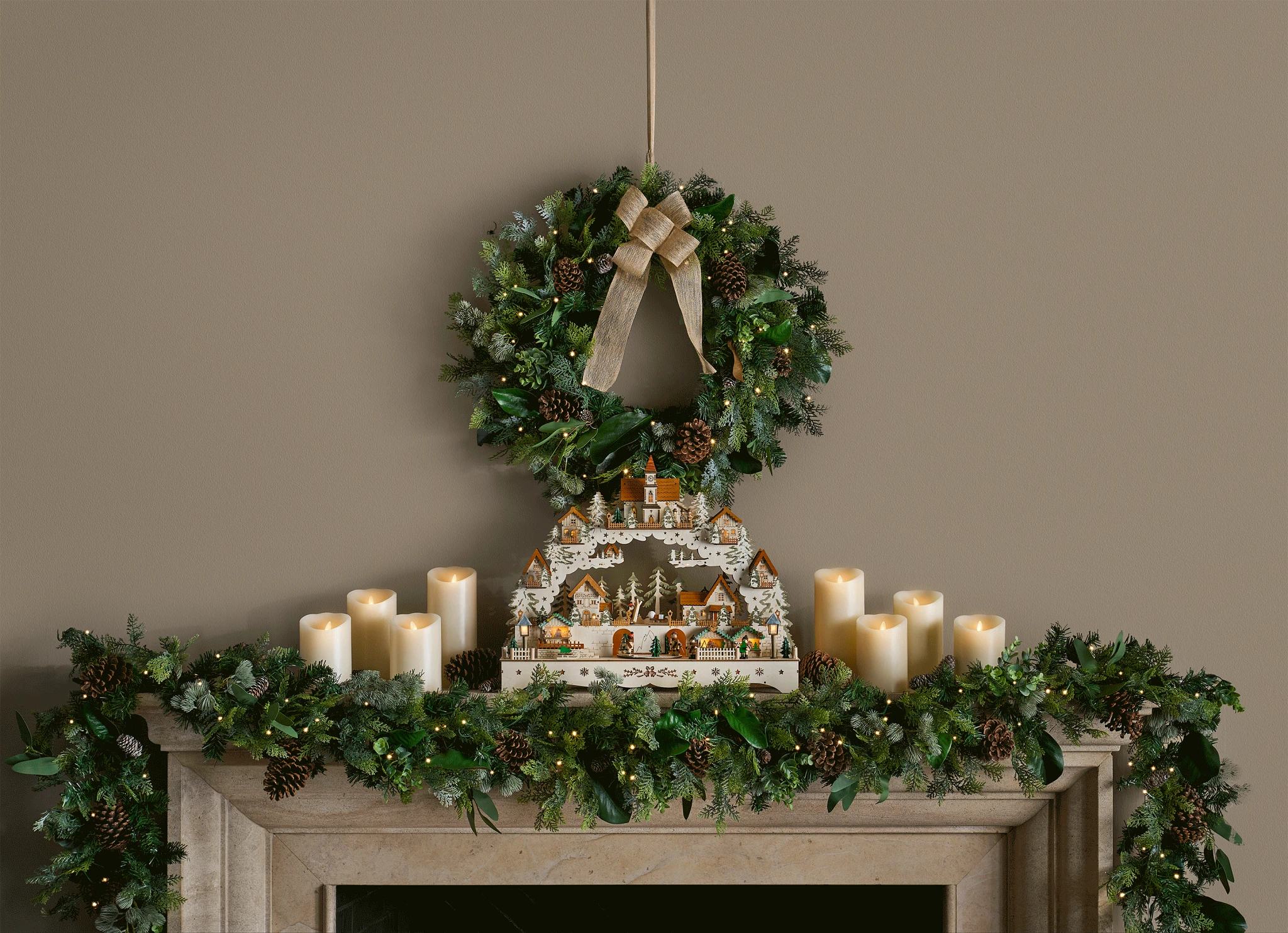 Mantel decorated with artificial greenery, candles, and animated Christmas village