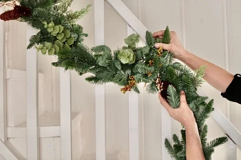 Woman hanging artificial Christmas garland on staircase handrails