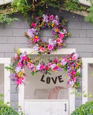 Facade of shed decorated with artificial spring wreath and garland featuring lavender, daisies, pomegranates, rose hips, purple hydrangeas, pink gerberas, mixed berries, and leaves