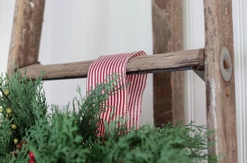 Artificial Christmas wreath with pinstriped ribbon hanging from a ladder