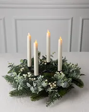 Ein Adventskranz mit vier weißen Kerzen, weißen Beeren und Zypressenblättern 
