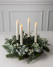 Ein Adventskranz mit vier weißen Kerzen, weißen Beeren und Zypressenblättern