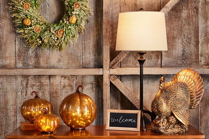 Thanksgiving table décor idea with pumpkins, turkey figurine, wreath, lamp, and chalkboard sign