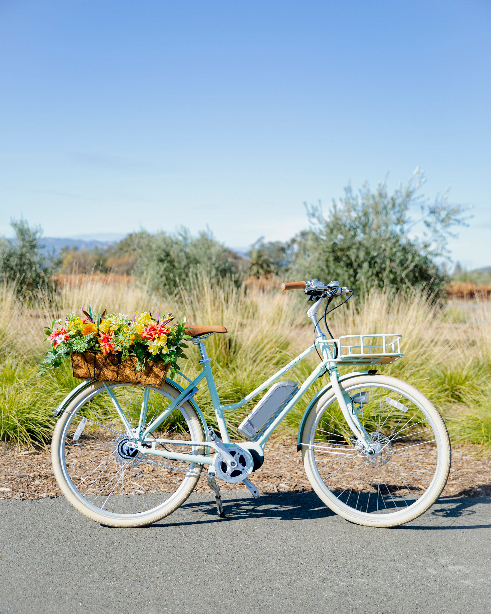 Bicycle decorated with artificial flower window box arrangement featuring faux dahlias, small daisies, carnations, ivy, and desert narrow leaves set on coconut fiber in an iron framed box 