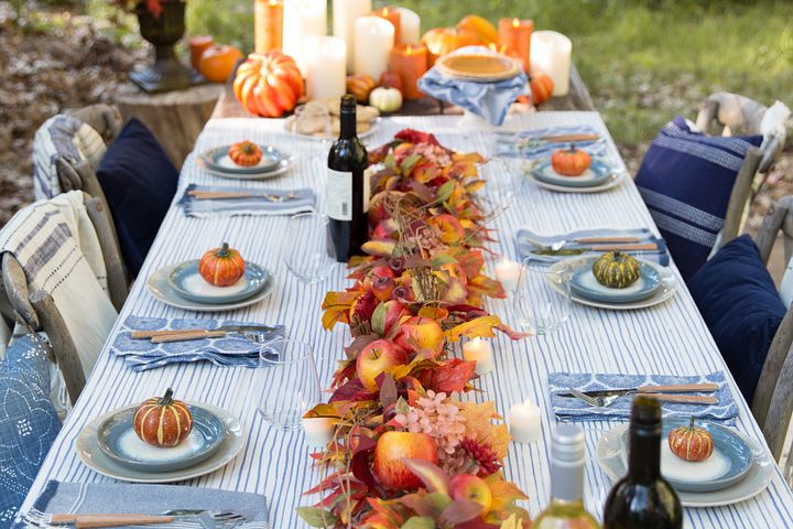Outdoor dining table decorated with candles, pumpkins, artificial fall garland, and blue and white place settings