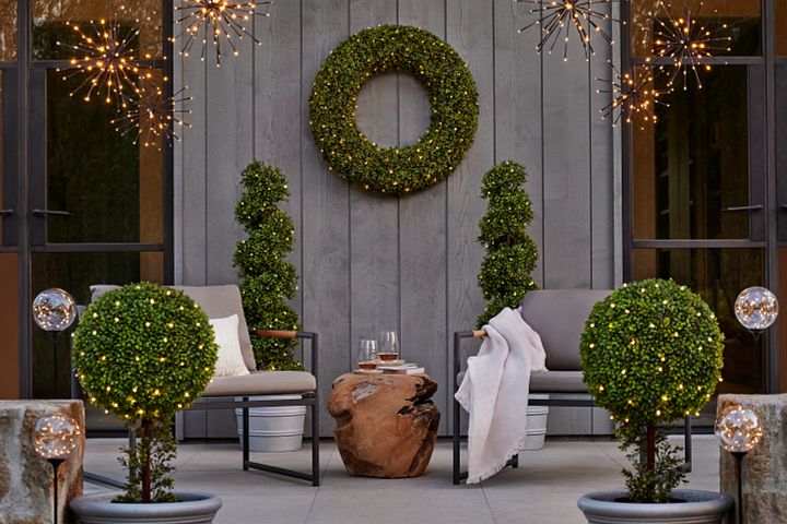An outdoor lounge setup with lit artificial topiary plants