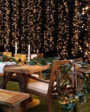 Outdoor dining table with artificial magnolia garland centerpiece and string lights in the background
