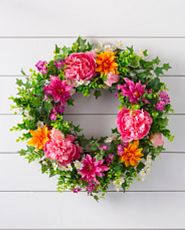 Artificial flower wreath with pink and orange peonies against a white background